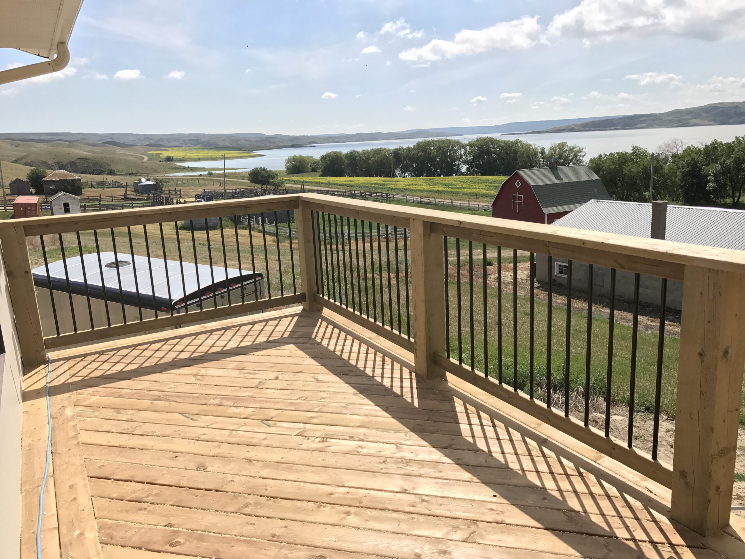 A spacious wood deck with a smooth, natural finish, surrounded by a lush green yard. The deck features clean lines and ample space, ideal for outdoor gatherings or relaxation.