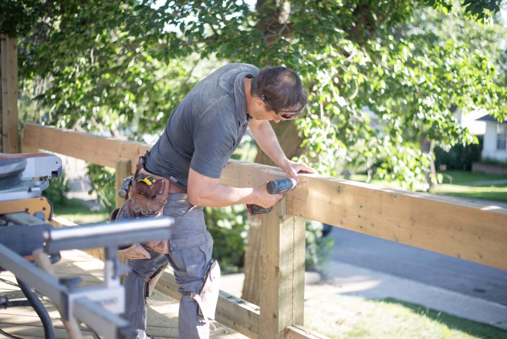 A skilled carpenter building a wooden deck, using tools to secure railings, representing Alberta Builder Services' expertise.