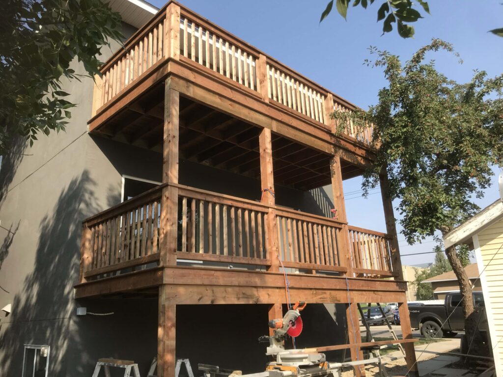 A two-story wooden deck with custom railings, under construction, showcasing Alberta Builder Services' craftsmanship.