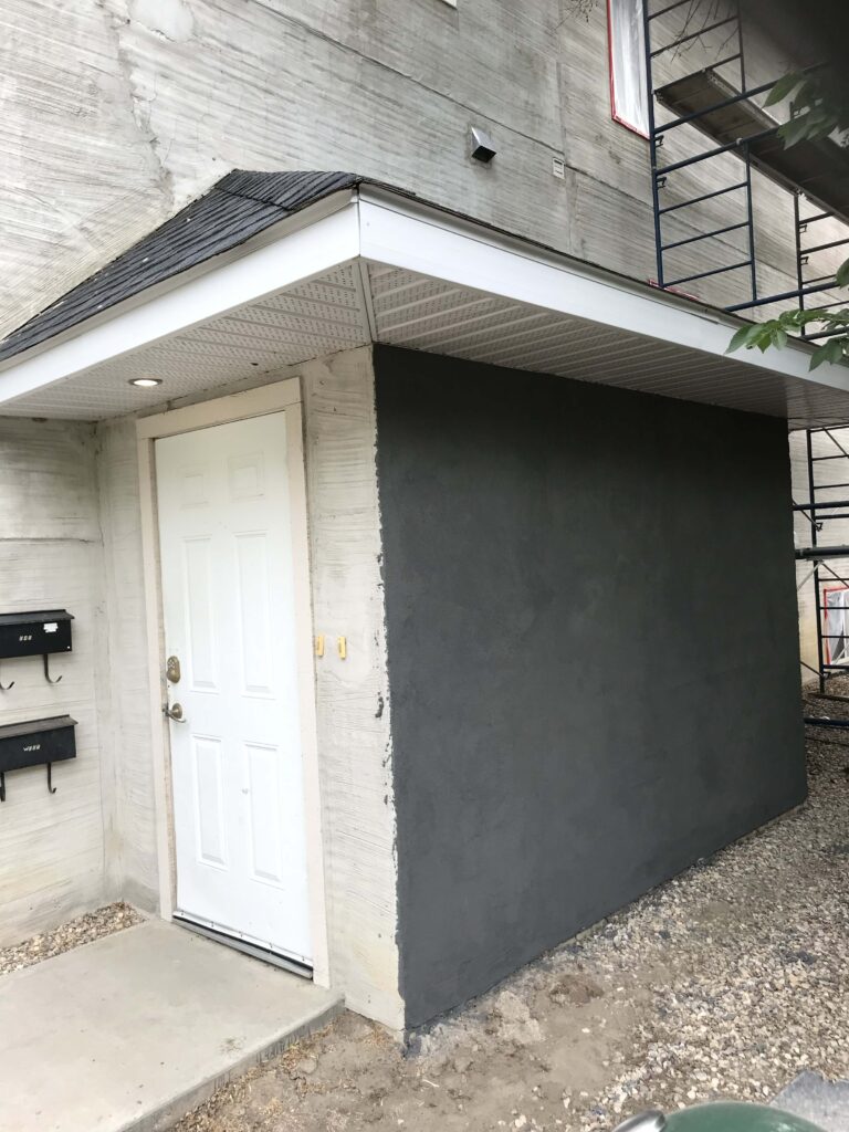 Side entrance of a home with a new grey stucco finish and a small overhang, showcasing custom construction by Alberta Builder Services.