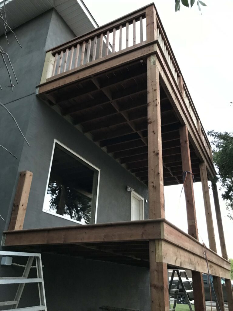 A custom-built two-level wooden deck attached to a modern grey stucco home, showcasing craftsmanship by Alberta Builder Services.