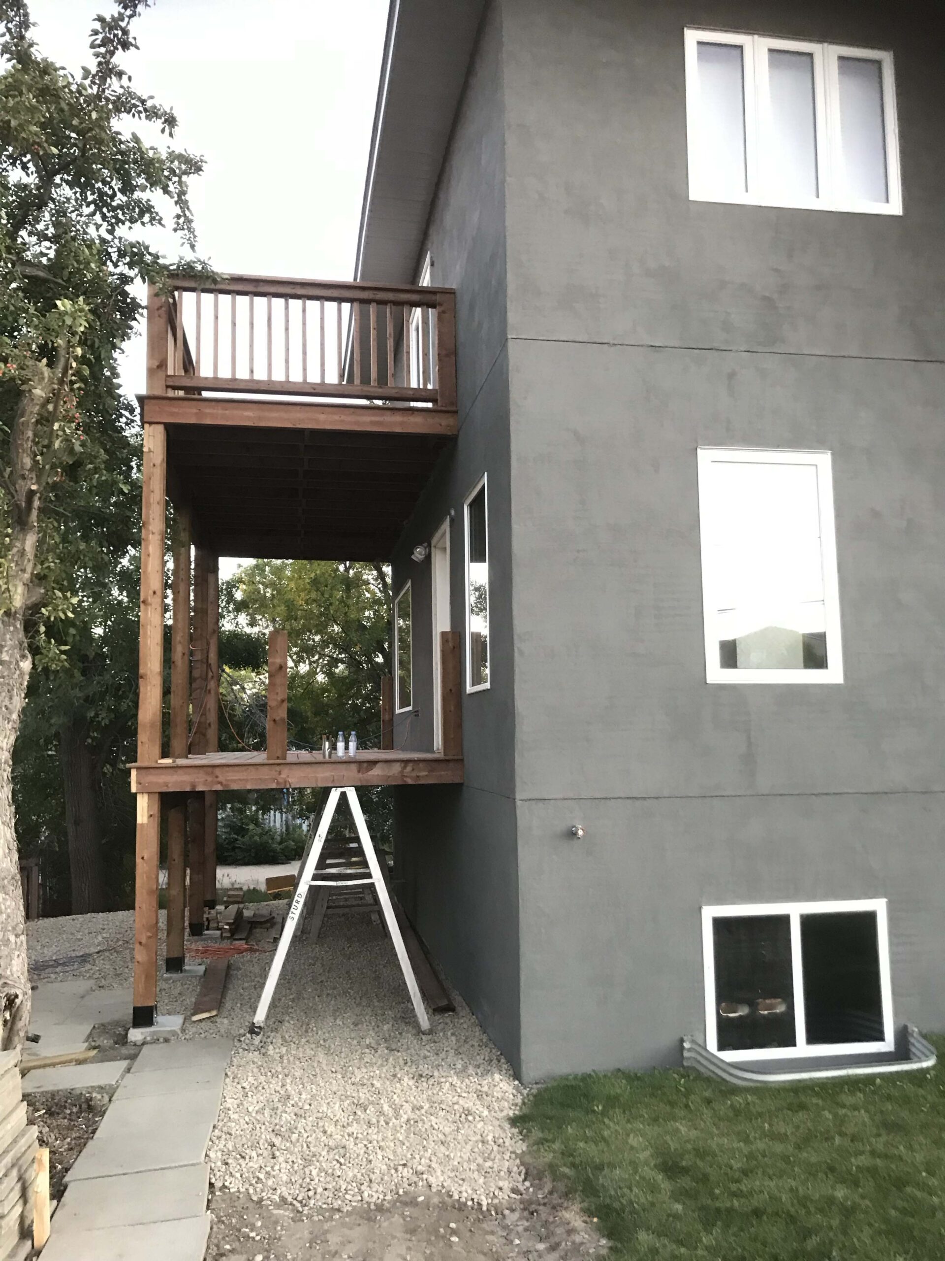 A modern home with a grey stucco exterior and a two-level wooden deck built by Alberta Builder Services.