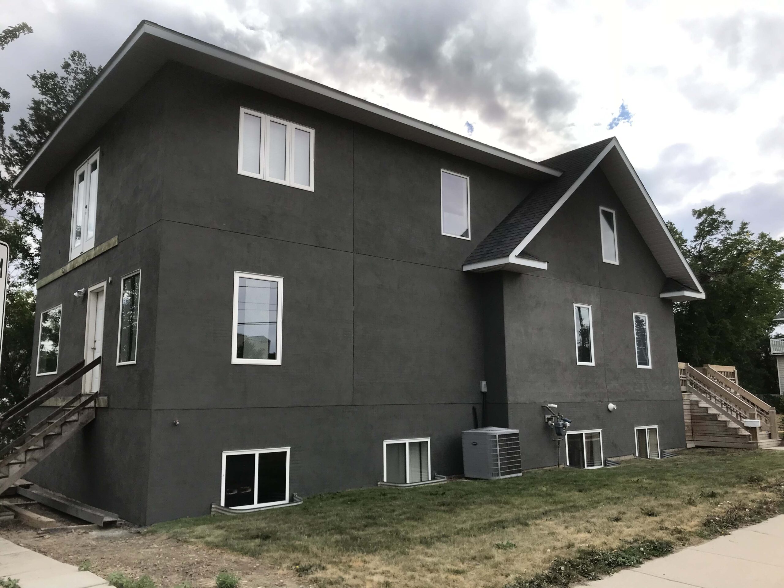 A modern two-story residential building with a sleek dark gray stucco finish, designed and completed by Alberta Builder Services.