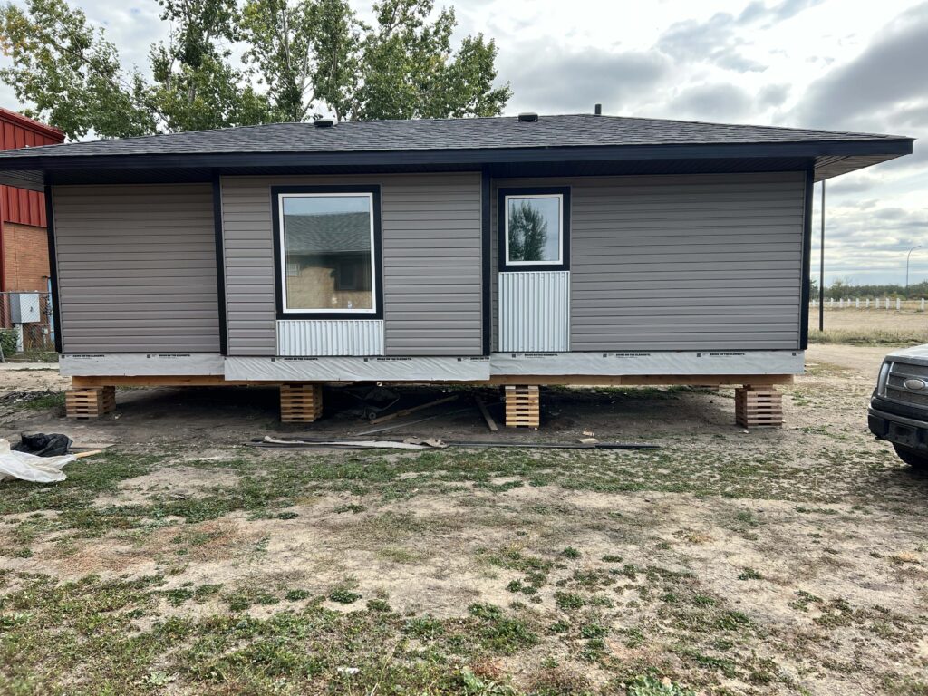 A residential home with newly installed light gray vinyl siding and a black trim finish, elevated on wooden supports during construction.