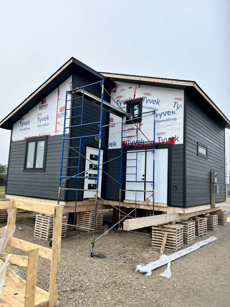 A small residential construction project featuring a home wrapped in Tyvek HomeWrap with partially installed dark siding.