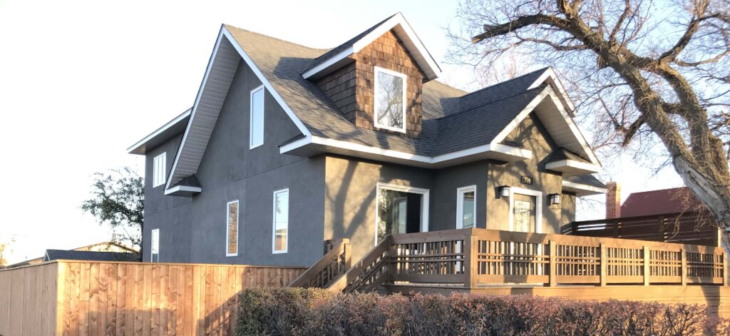 A fully renovated home featuring modern stucco exterior, a wooden deck, and custom fencing, showcasing craftsmanship by Alberta Builder Services.