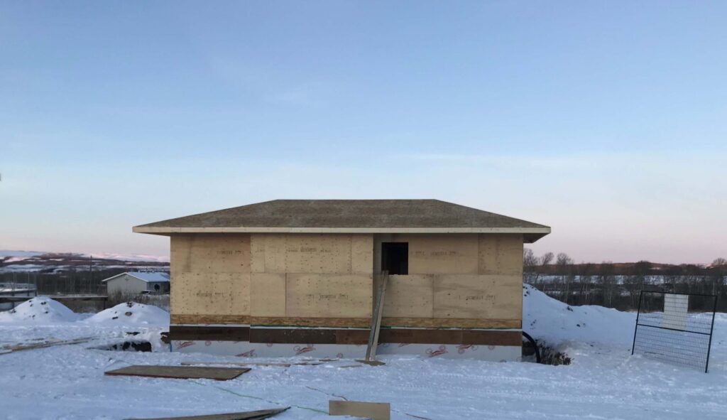 A framed house under construction in a snowy landscape, built by Alberta Builder Services, showcasing expertise in custom solutions.