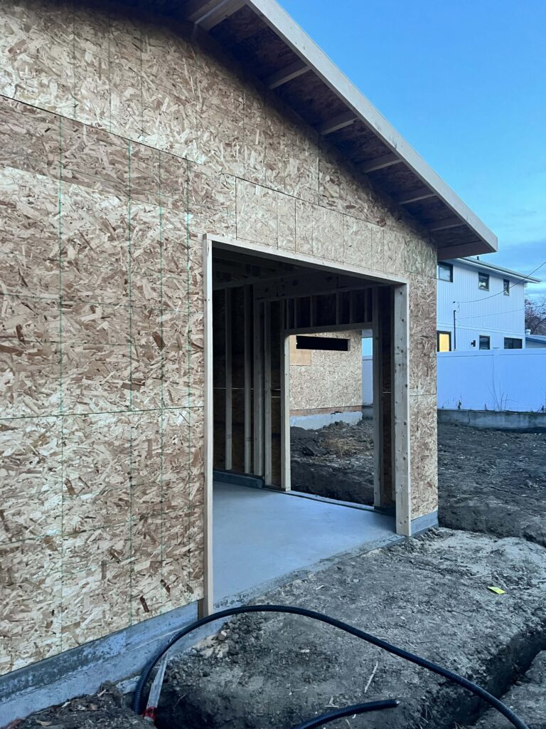 A partially constructed garage with framed walls, a roof, and a doorway, built by Alberta Builder Services.