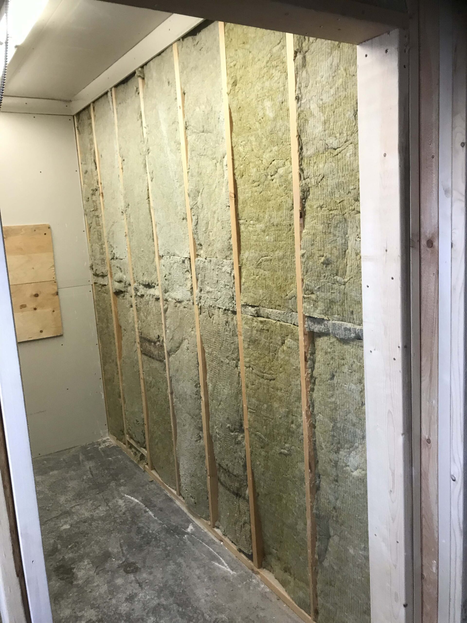 Close-up of a partially insulated wall with exposed wood framing, showcasing Alberta Builder Services' expertise in custom construction and insulation solutions.