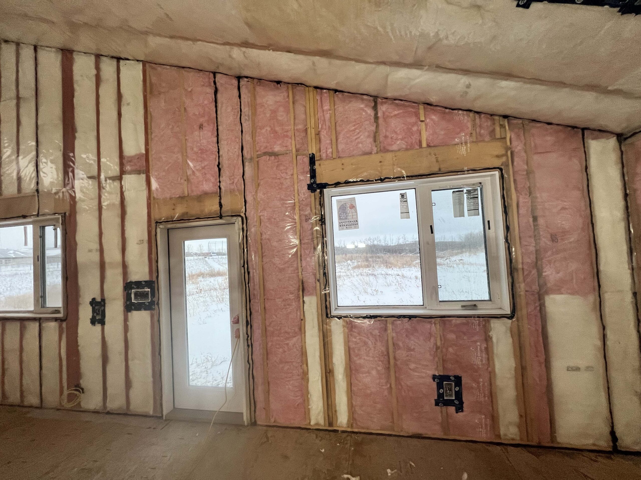 Interior view of a custom-built structure with installed insulation, windows, and a door, demonstrating Alberta Builder Services' precision and expertise in construction.