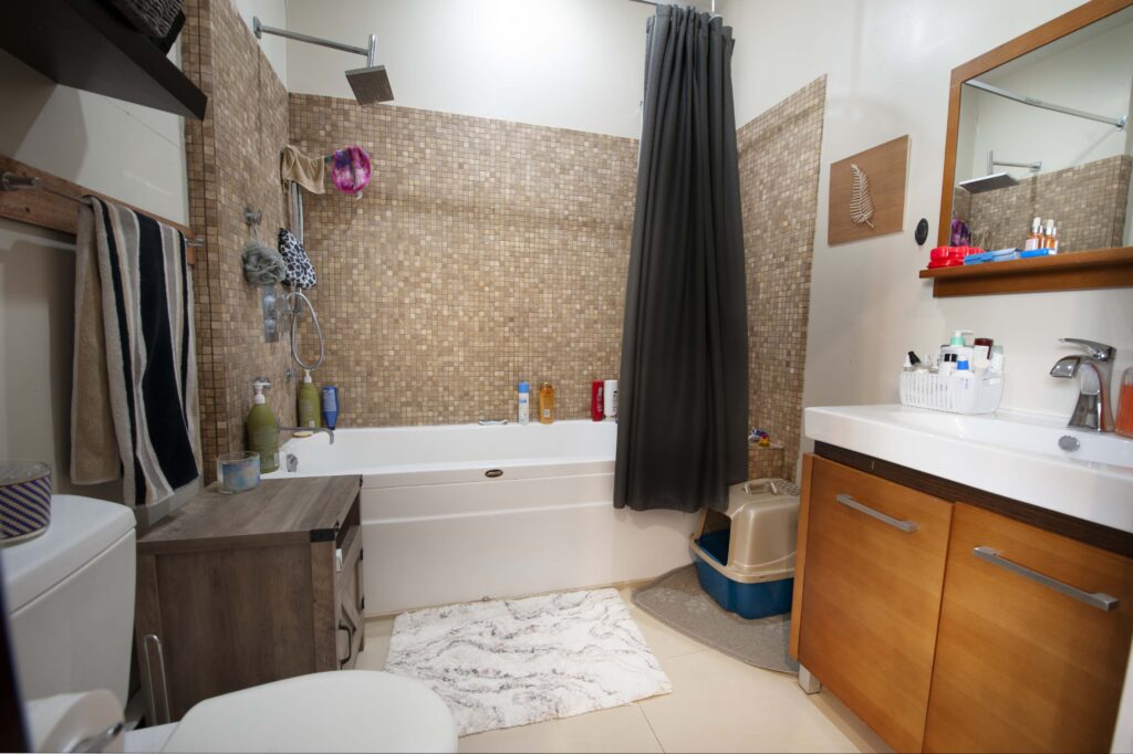 Renovated bathroom featuring modern tiled walls, soaking tub with rainfall showerhead, wood-finish vanity, and contemporary fixtures.