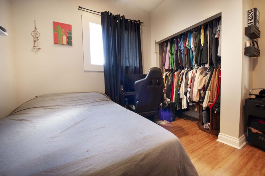 Basement suite bedroom with a cozy setup including a bed, open closet, and workspace.