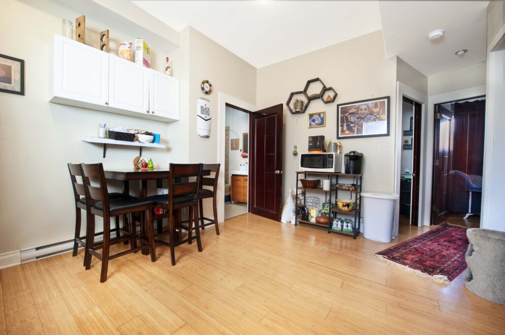 Modern basement suite dining area featuring a dark wood dining set, bamboo flooring, and practical shelving.