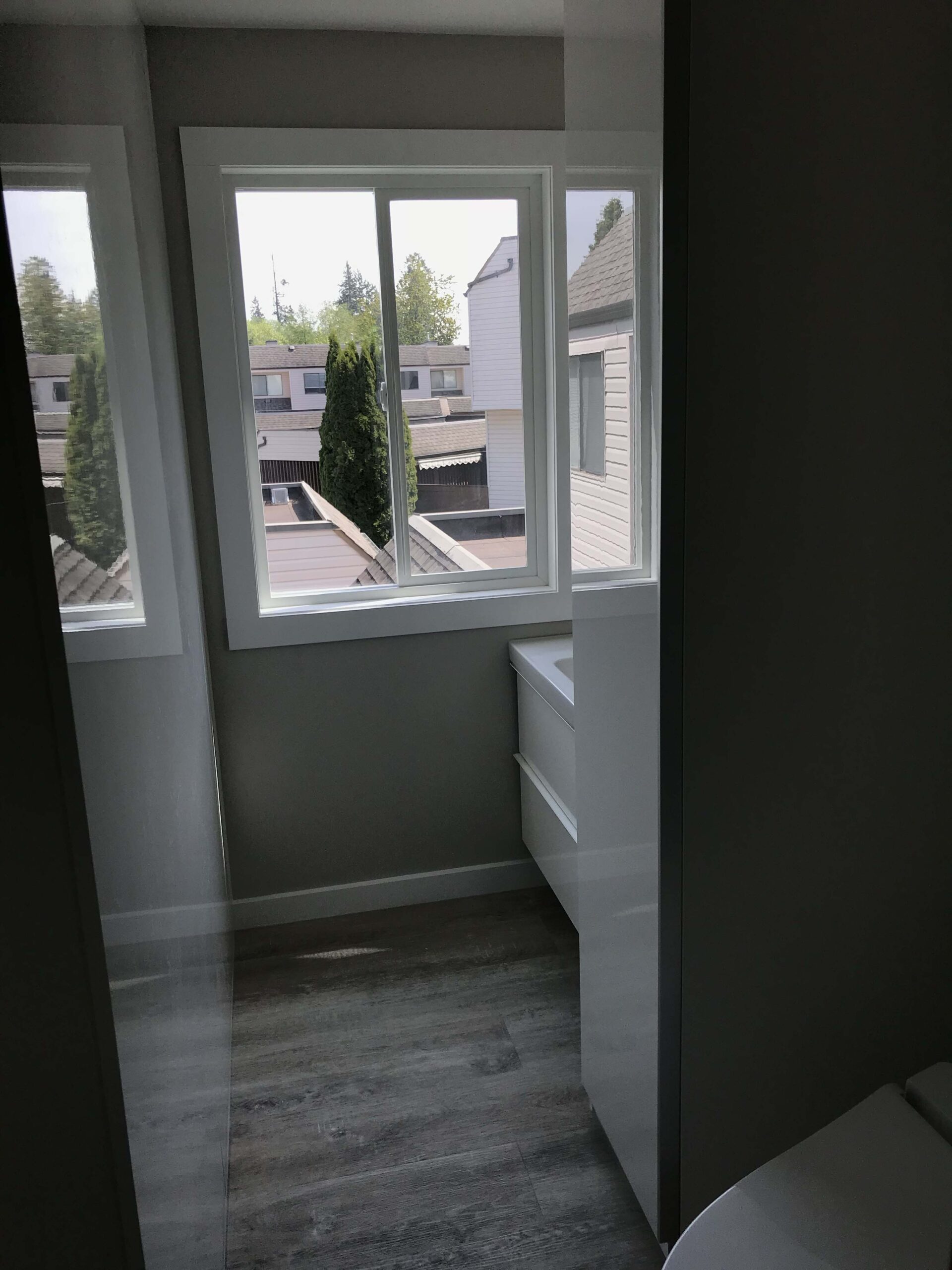 A modern bathroom with large windows providing ample natural light, featuring sleek flooring and a compact vanity unit.