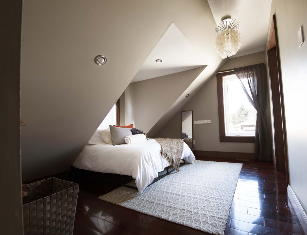 Modern attic bedroom with sloped ceiling, wood accents, and a cozy design by Alberta Builder Services.