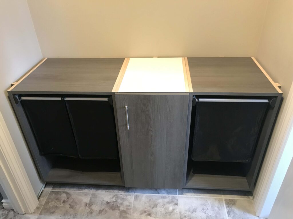 Custom laundry room cabinetry with a modern grey wood finish, featuring built-in pull-out hampers and sleek design.