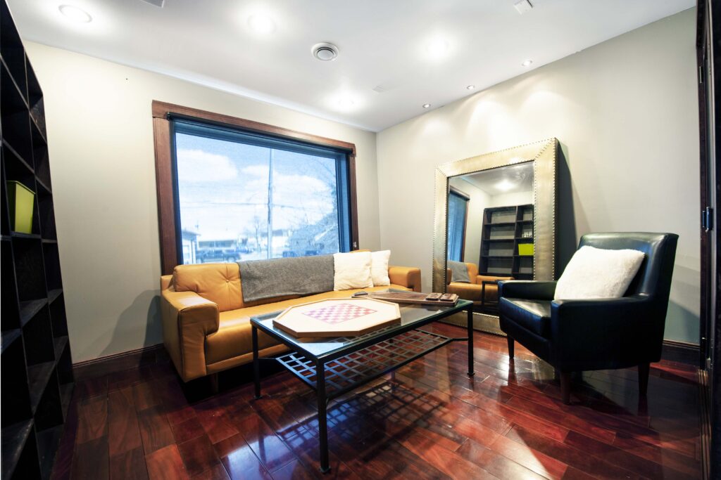 Modern renovated den with custom finishes, featuring a leather sofa, armchair, and large mirror by Alberta Builder Services.