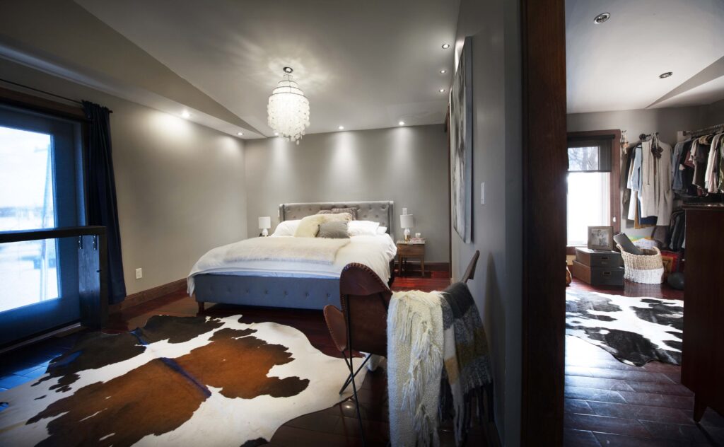 Modern master bedroom with a chandelier, upholstered bed, cowhide rug, and adjacent walk-in closet.