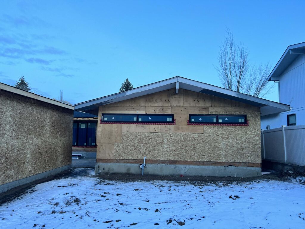 Renovated exterior wall with modern windows, plywood sheathing, and clean framing under a blue evening sky.