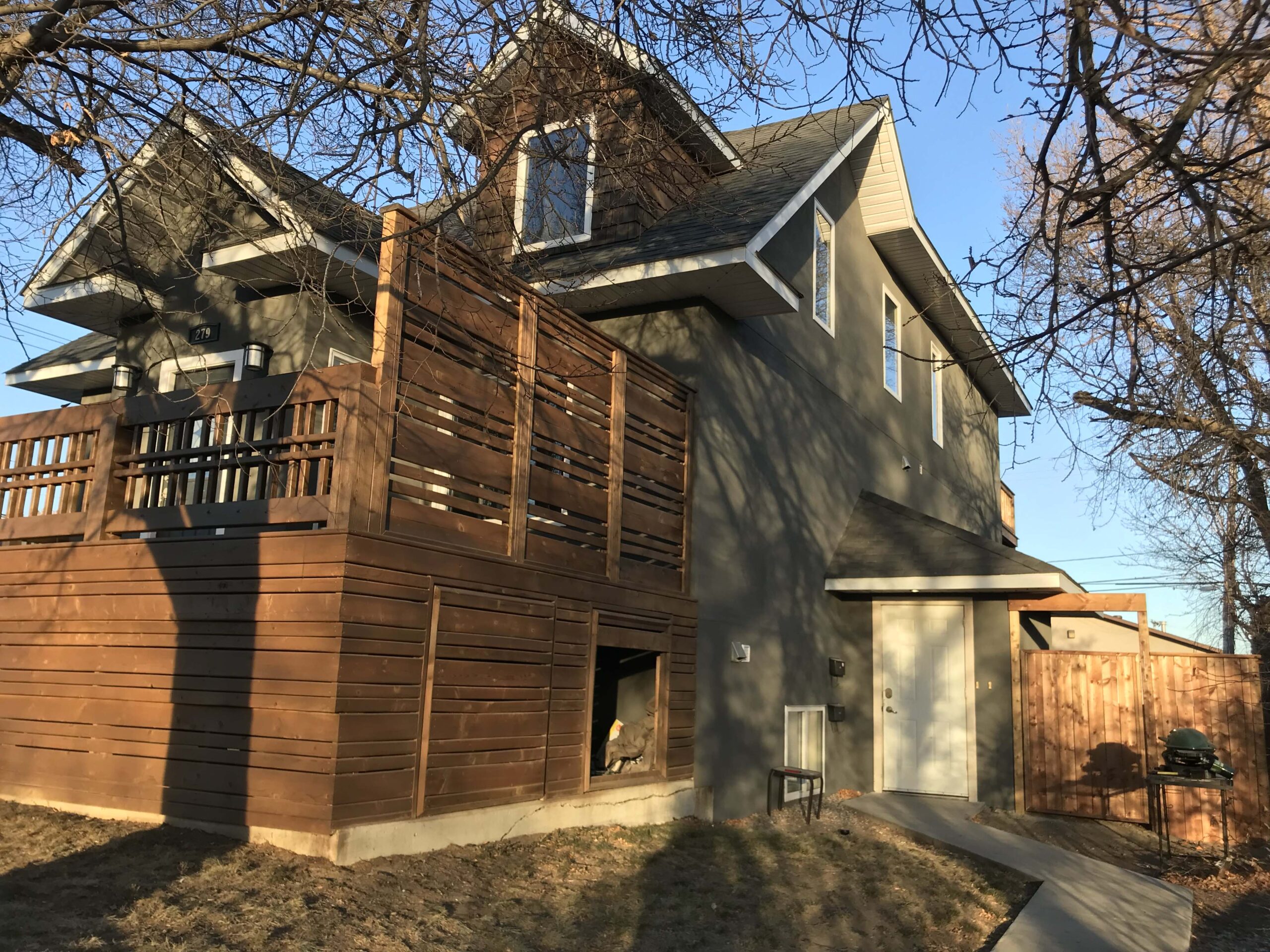 A large wooden deck with privacy panels and built-in storage, attached to a modern home, built by Alberta Builder Services.