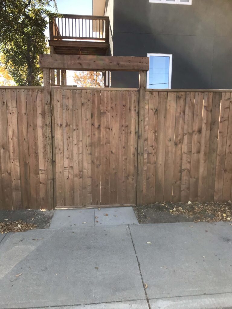 A custom-built wooden fence with a pedestrian gate, constructed by Alberta Builder Services, showcasing durability and an elegant natural finish.