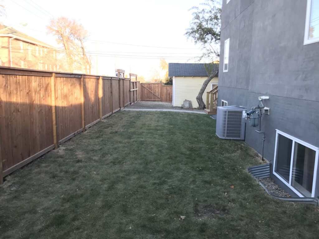 Backyard view of a custom-built wooden fence installed by Alberta Builder Services, with a neatly maintained lawn and a secure double gate at the far end.