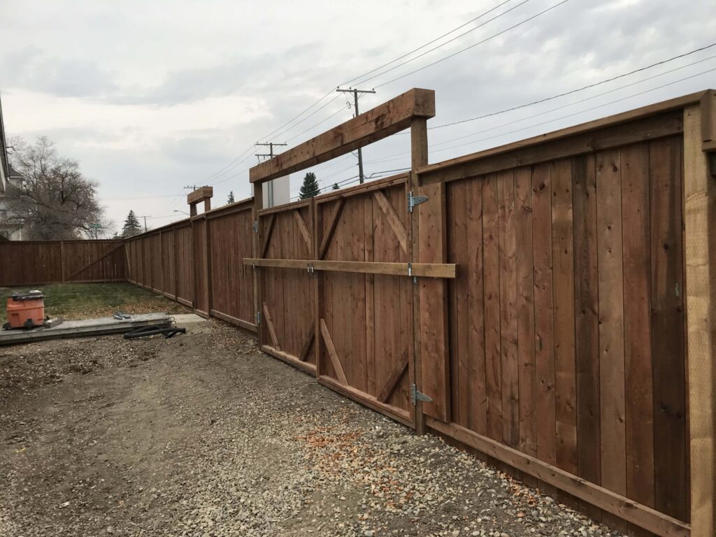 Custom-built wooden fence with a large double gate, featuring robust construction and high-quality materials in a residential backyard.