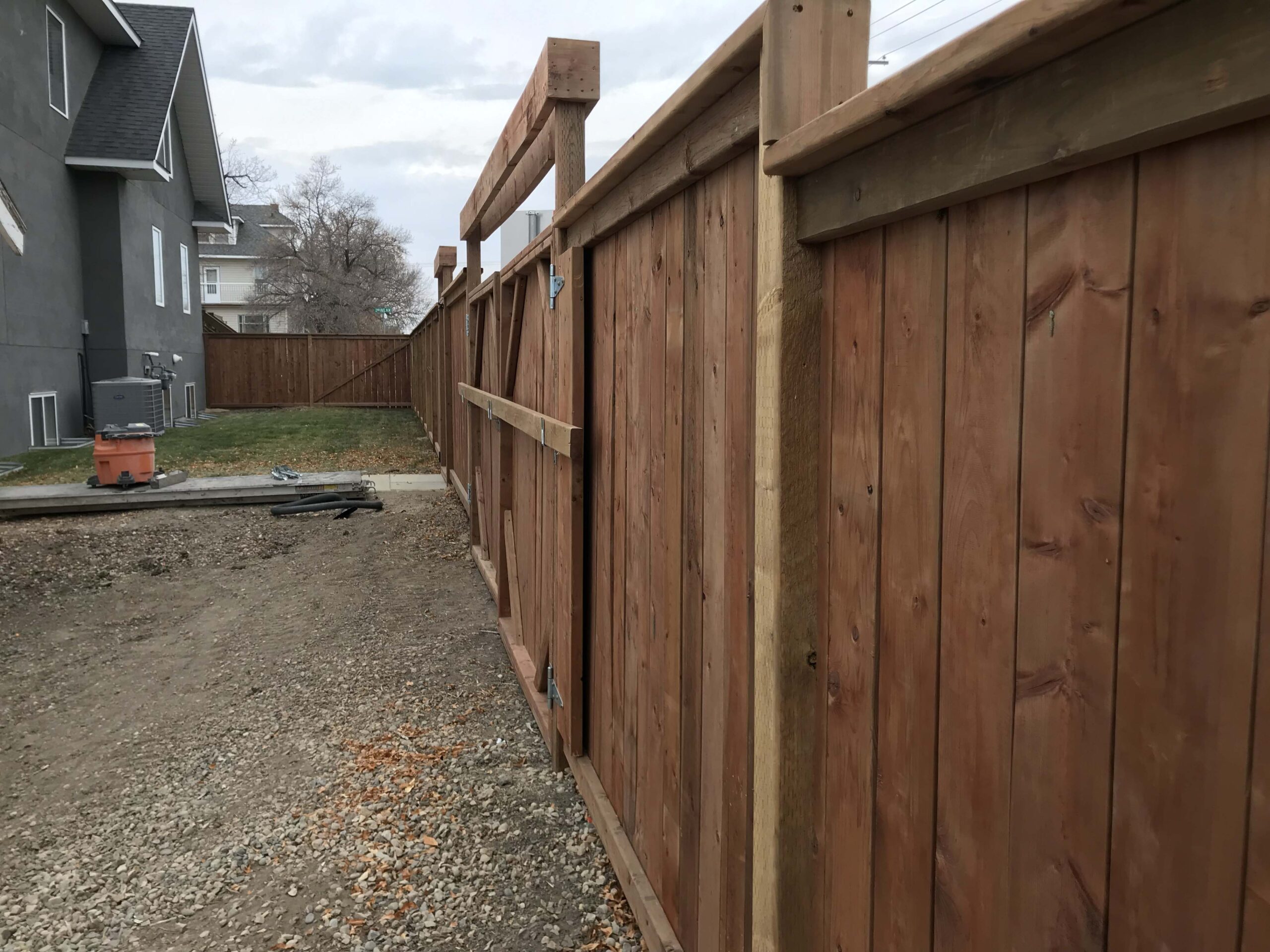 Completed custom wooden fence with a large gate, showcasing detailed craftsmanship in a residential backyard.