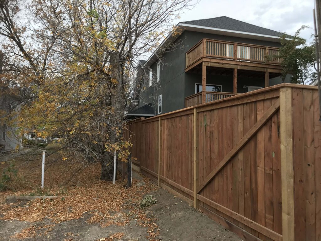 Completed wooden privacy fence with a sturdy design enclosing a backyard, with a two-story house and trees in the background.