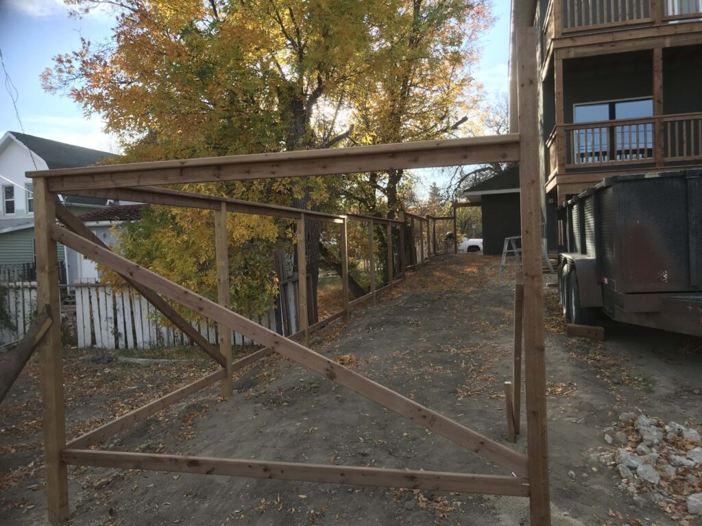 Wooden fence framing structure under construction with autumn trees in the background.