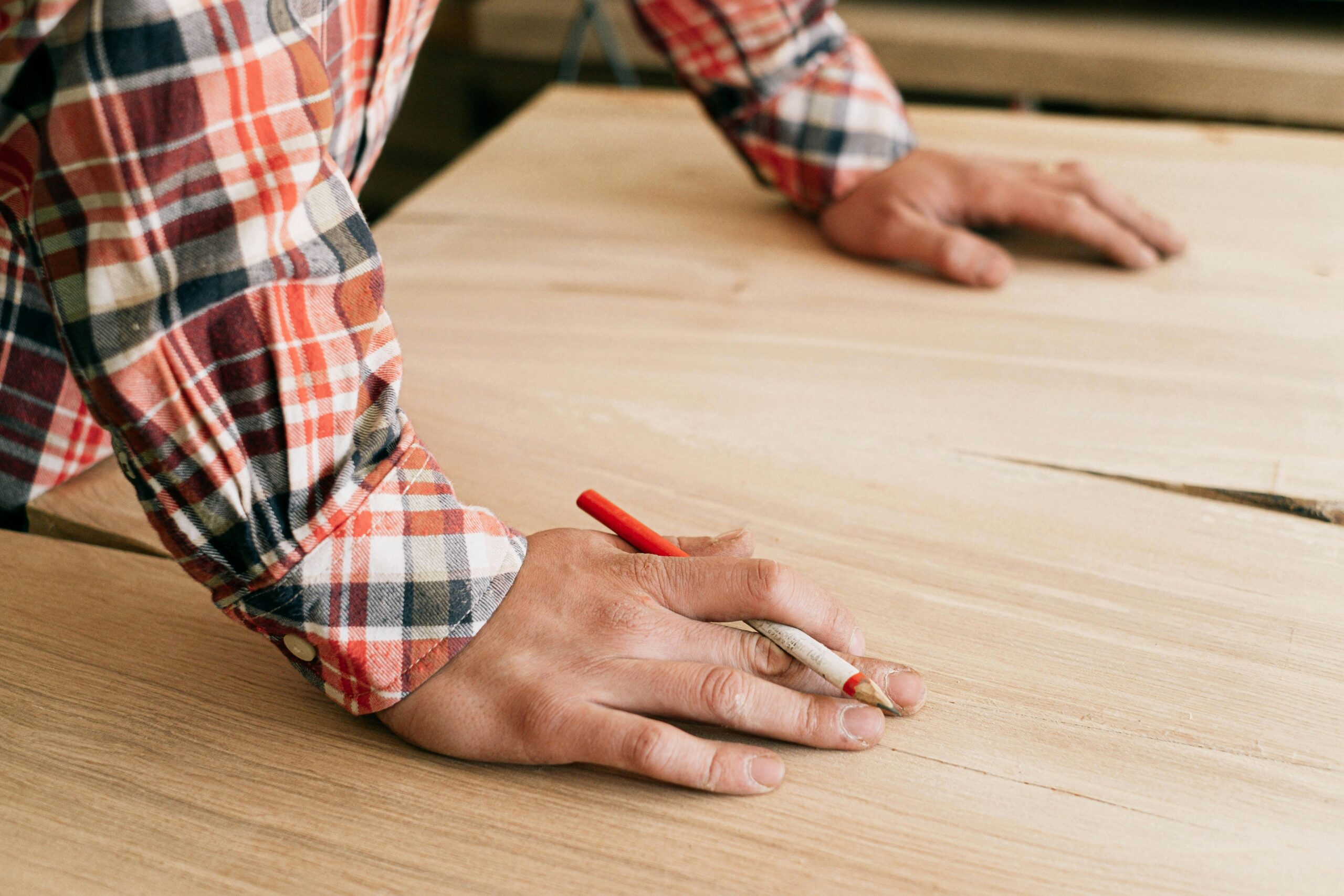 Carpenter using a red pencil to mark woodworking design plans, a key part of custom deck and garage projects by trusted garage and deck specialists.