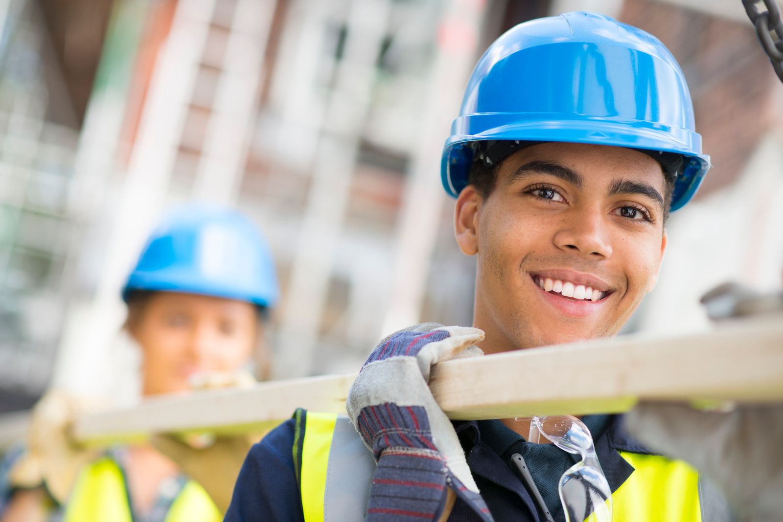 Smiling construction worker with blue helmet and safety gear, showcasing a career with Alberta Builder Services Ltd.