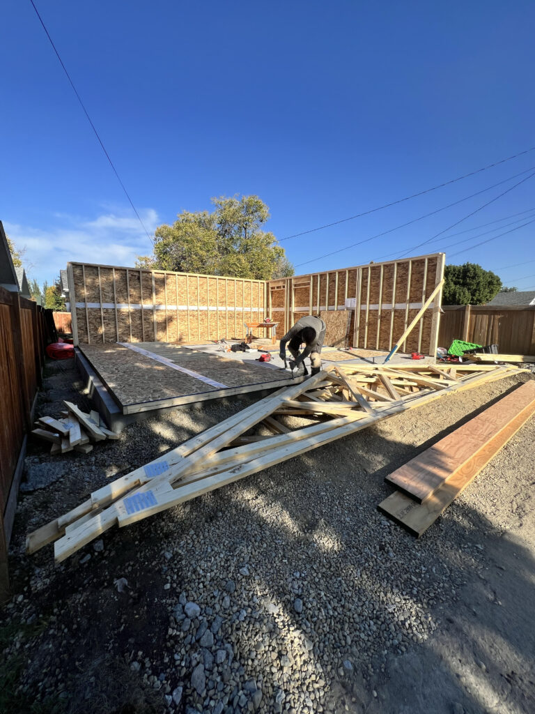 Framing in progress for a detached garage in Edmonton, showing exterior walls being assembled and trusses staged for installation by Alberta Builder Services Ltd.