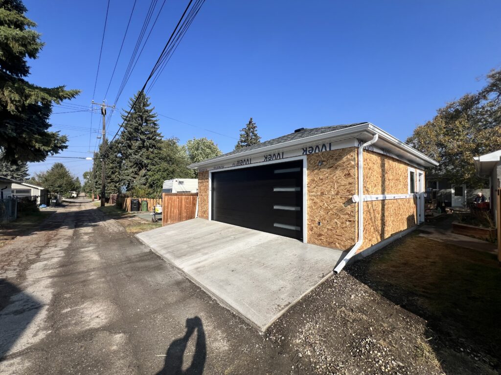 Completed detached garage in Edmonton with black overhead door, concrete driveway apron, and finished roofing by Alberta Builder Services Ltd.