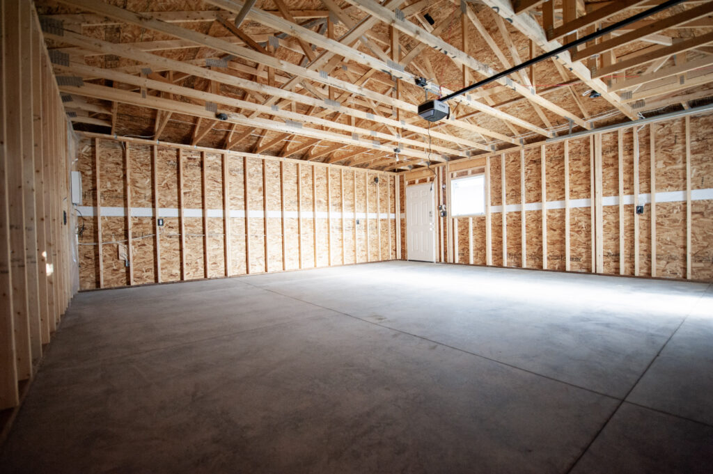 Interior of an unfinished garage showing exposed framing, open trusses, concrete floor, and installed electrical wiring.