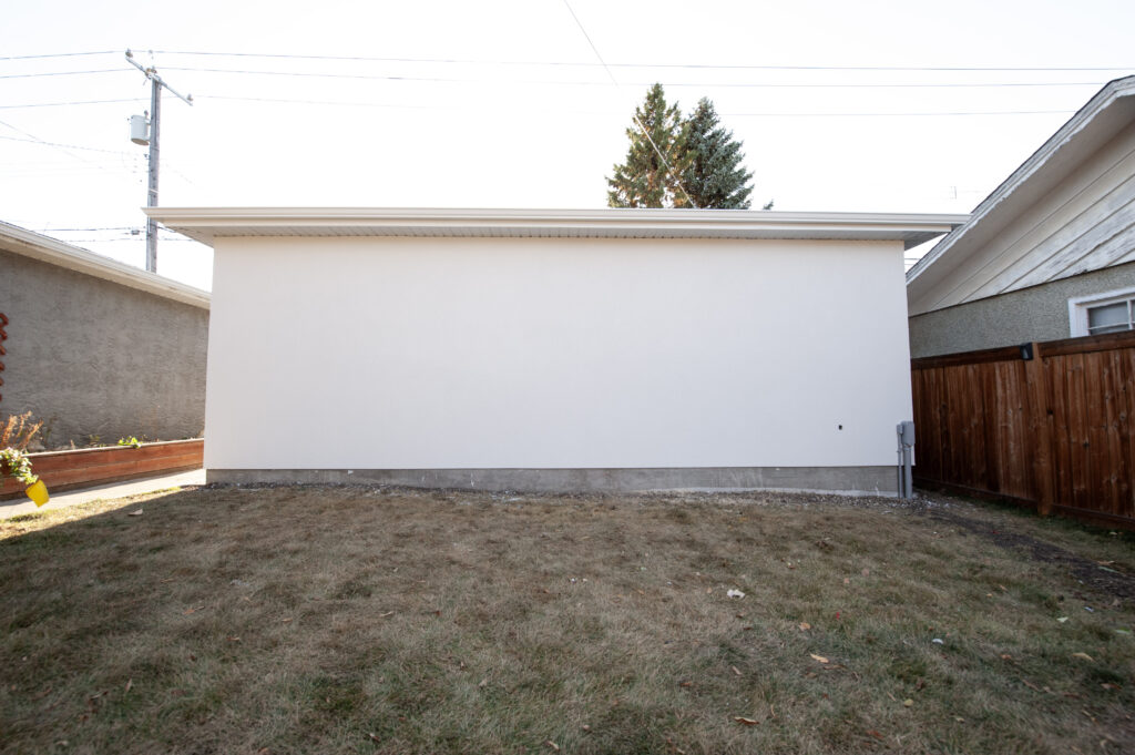 Back view of a completed detached garage with smooth acrylic stucco finish and landscaped yard.
