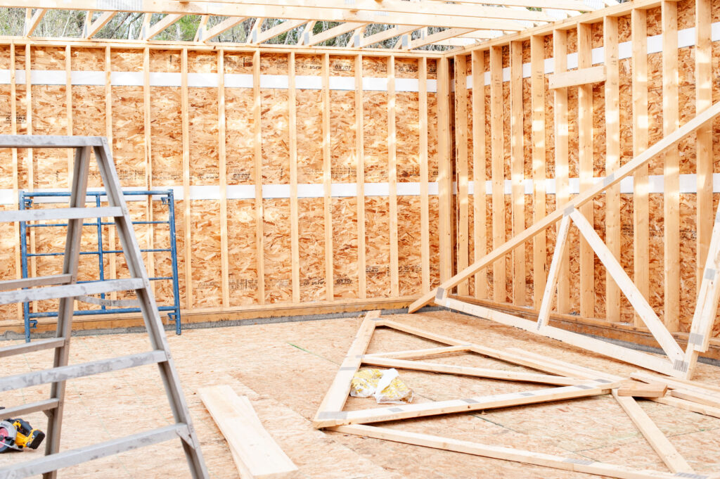 Interior view of a framed garage under construction with OSB sheathing, wall studs, roof trusses, and construction tools visible.