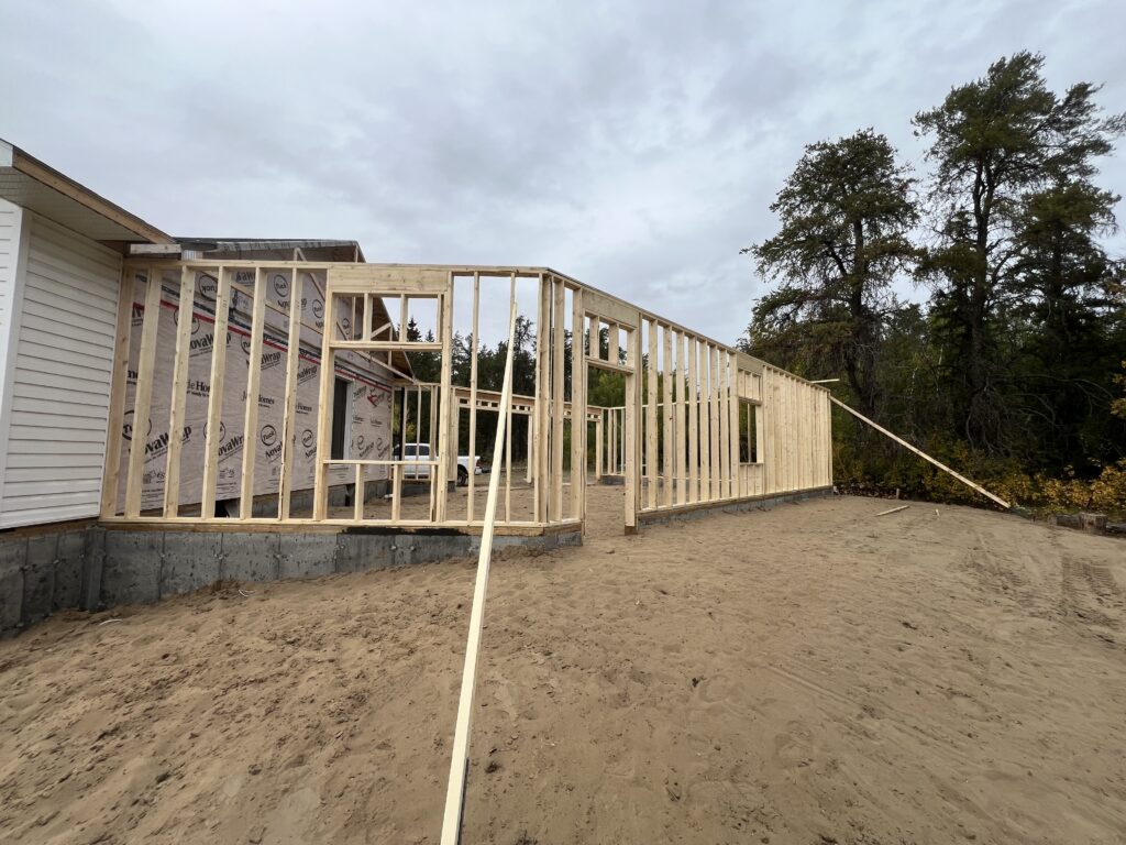 Framed exterior walls of a new garage under construction beside a house, with sand base and bracing supports visible.