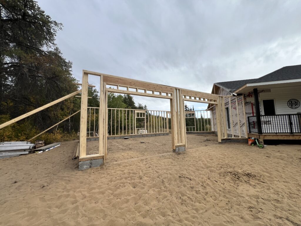 Framed garage entrance with rough openings for double overhead doors beside a home under construction on a sandy lot.