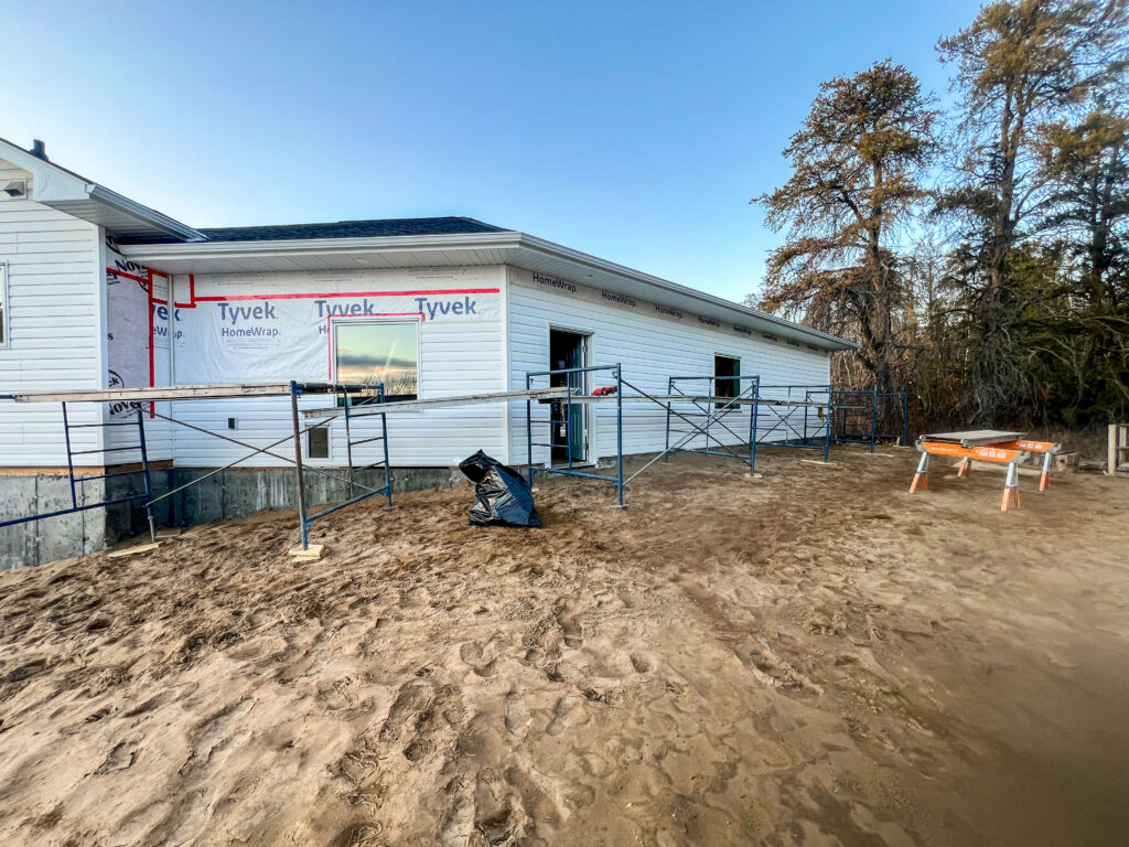 Exterior view of an attached garage under construction with scaffolding set up along the wall and Tyvek wrap visible around window and door openings.