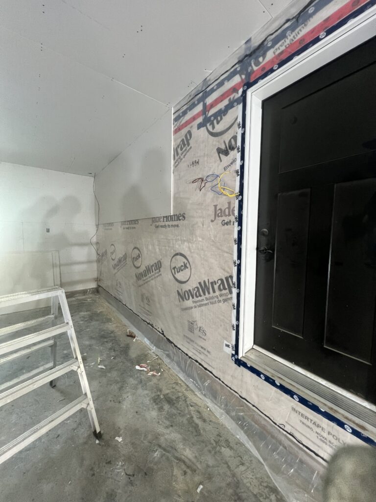 Interior construction photo showing drywall installation and building wrap around a door frame.