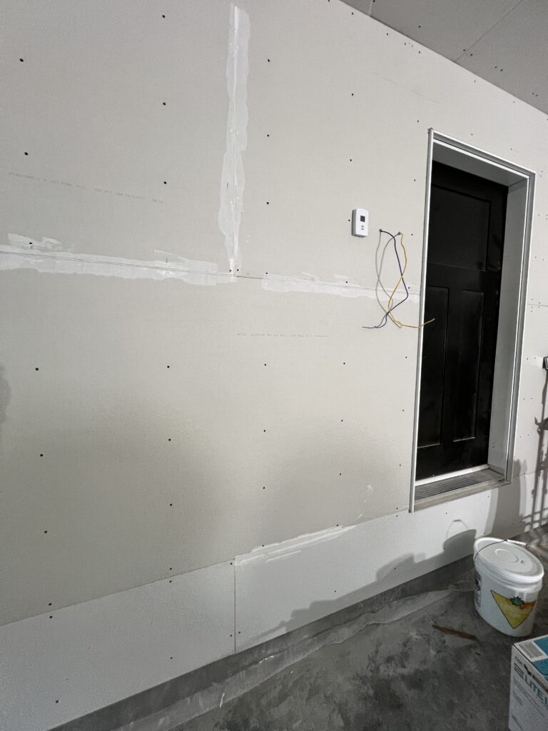 Drywall installation with taped seams and mudding in progress beside an exterior door.