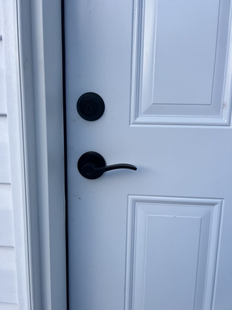 Close-up of a white exterior door with a matte black lever handle and deadbolt lock.