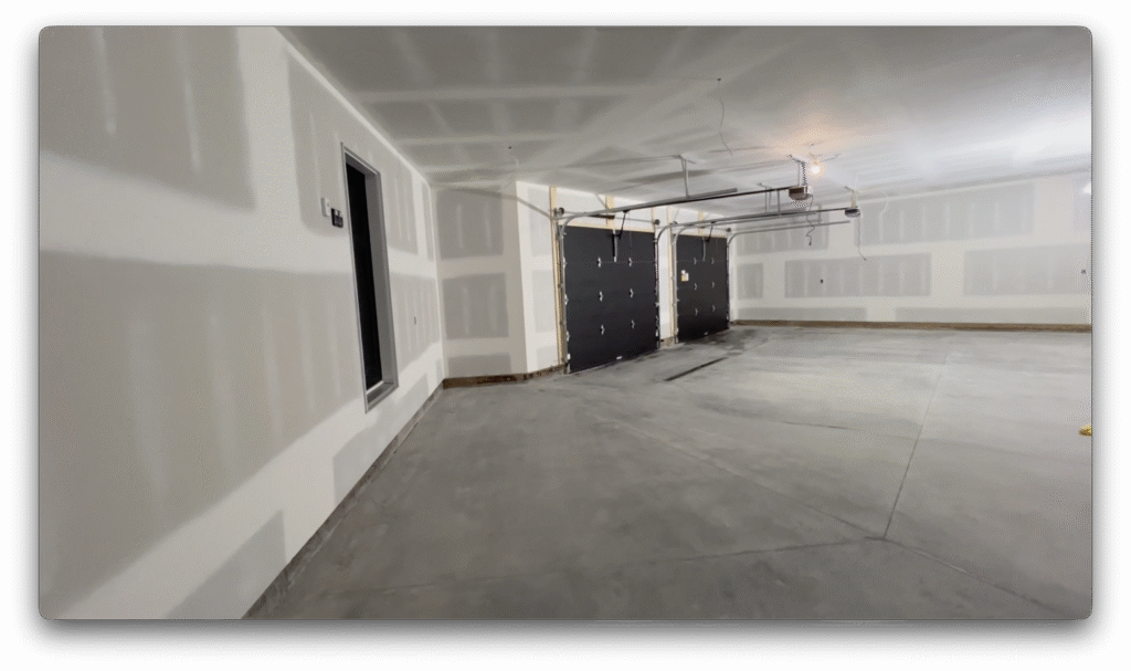 Finished garage interior with drywall completed, dual black overhead doors, and smooth concrete floor.