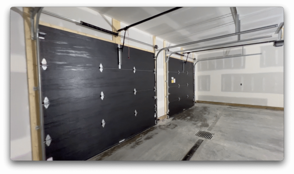 Two black insulated garage doors installed inside a finished garage with concrete flooring and drywall.