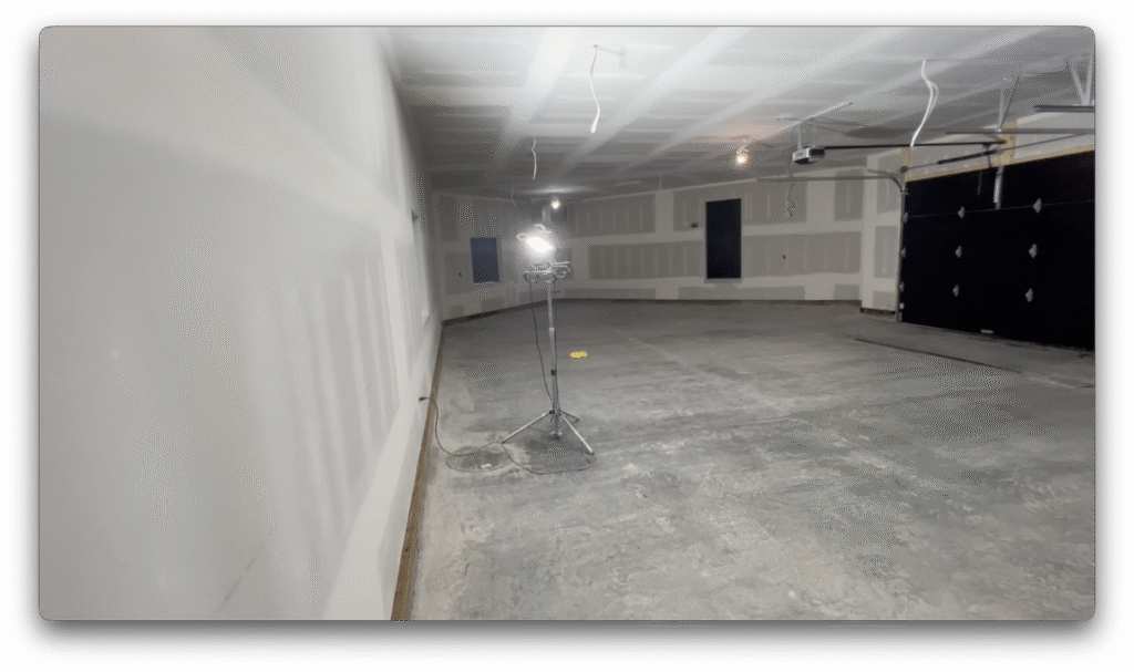 Finished garage interior with taped drywall, concrete floor, temporary work light, and installed garage doors.