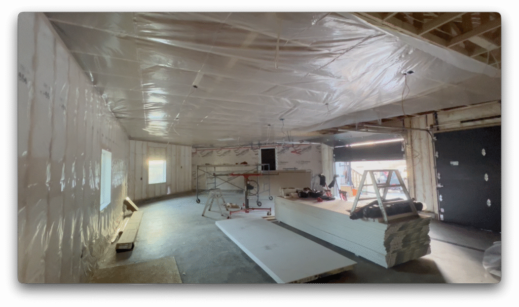 Garage under construction with insulation, vapor barrier, stacked drywall, and scaffolding prepared for installation.