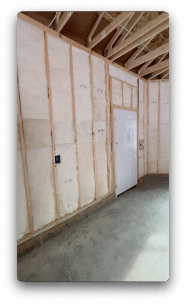 Insulated garage wall with exposed framing, a white exterior door, and unfinished concrete floor.