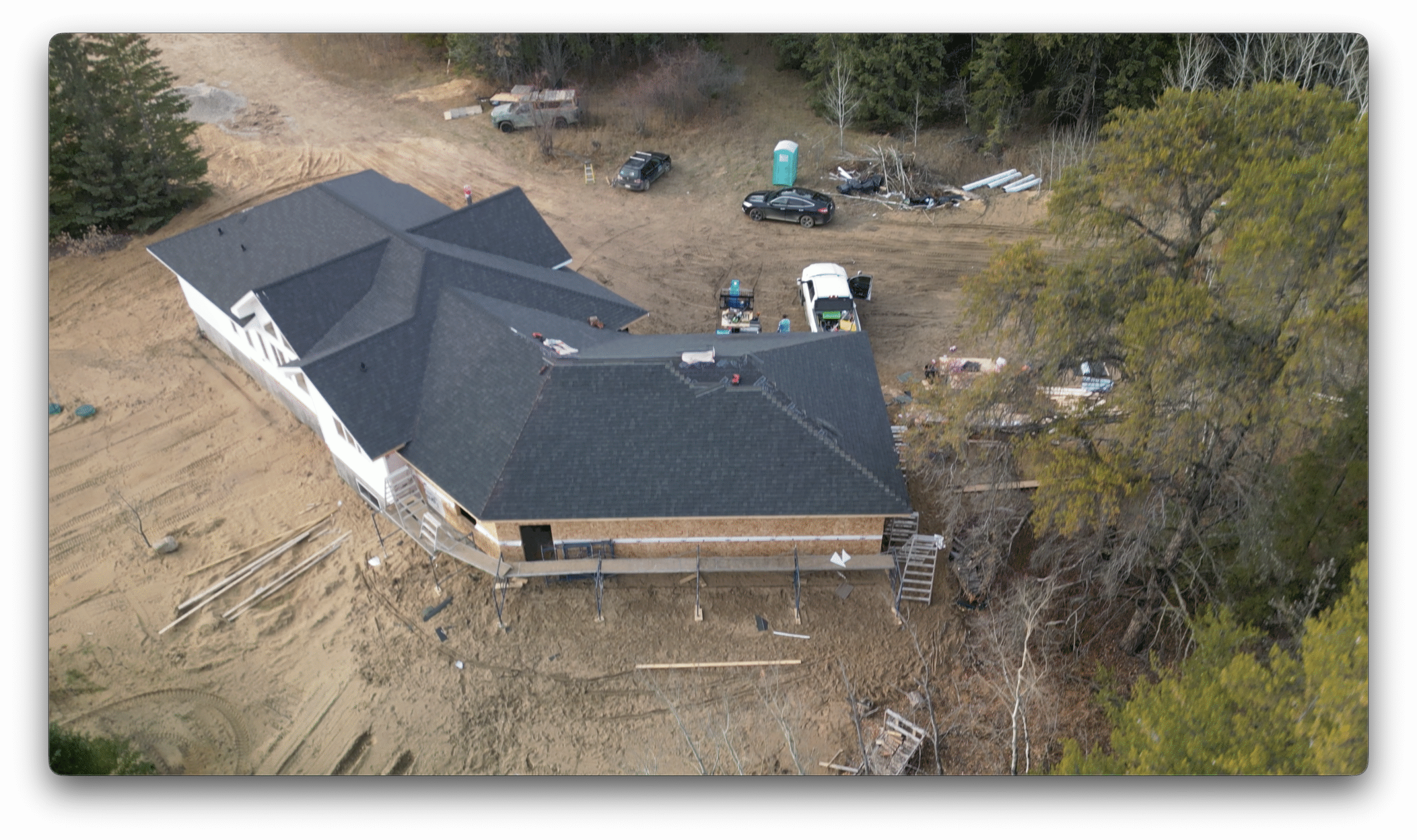 Drone photo showing a residential construction site with shingles being installed on the roof and work vehicles, scaffolding, and materials surrounding the home.