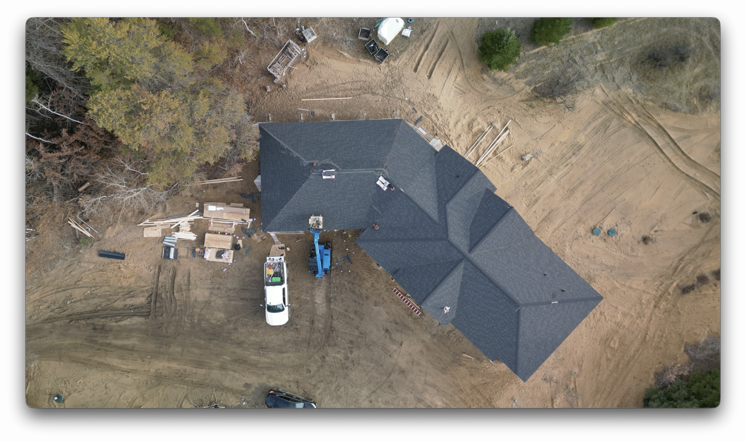 A top-down drone image of a residential construction site showing completed roof shingles, construction vehicles, and building materials around the home.